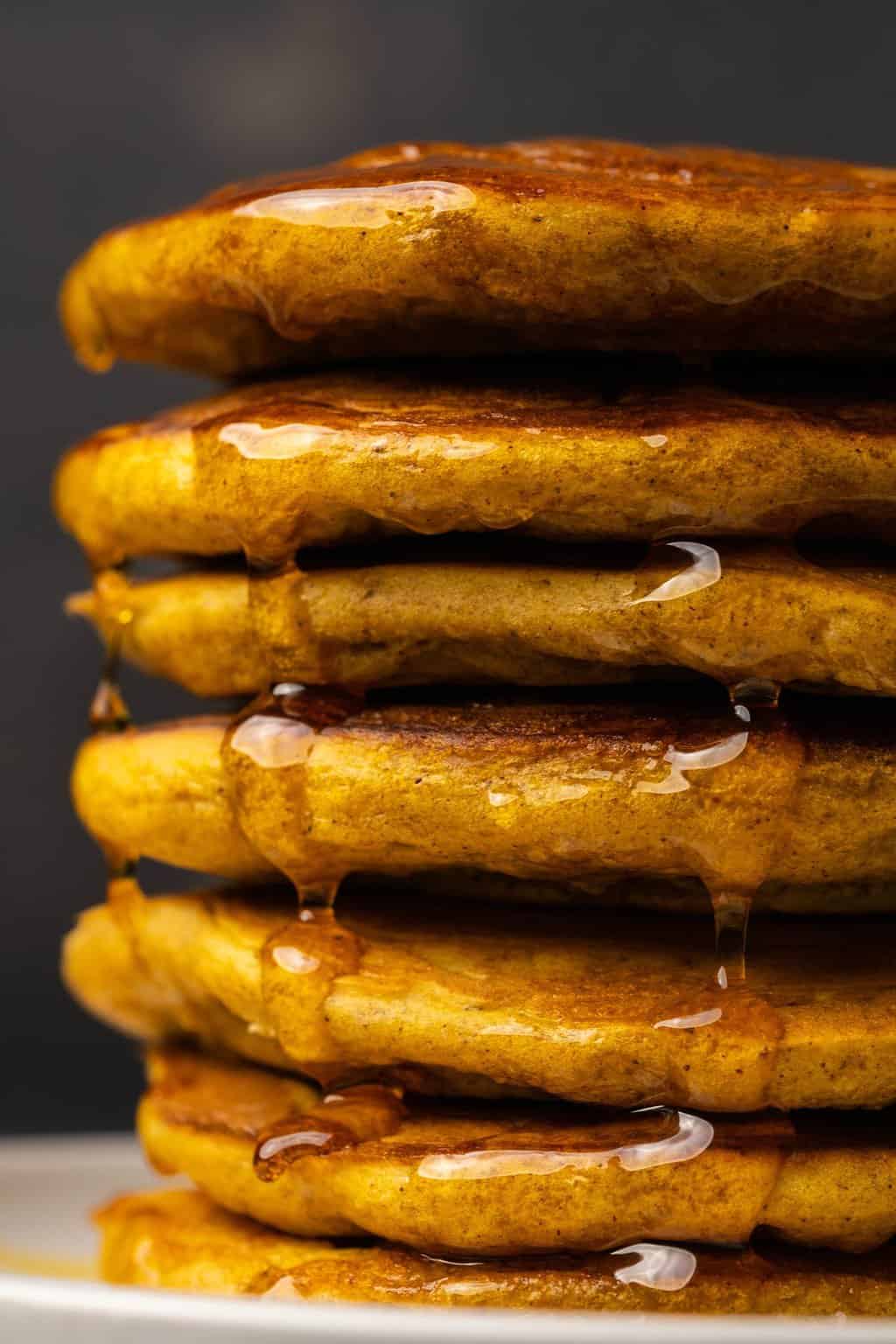 A stack of vegan pumpkin pancakes drizzled with syrup. 