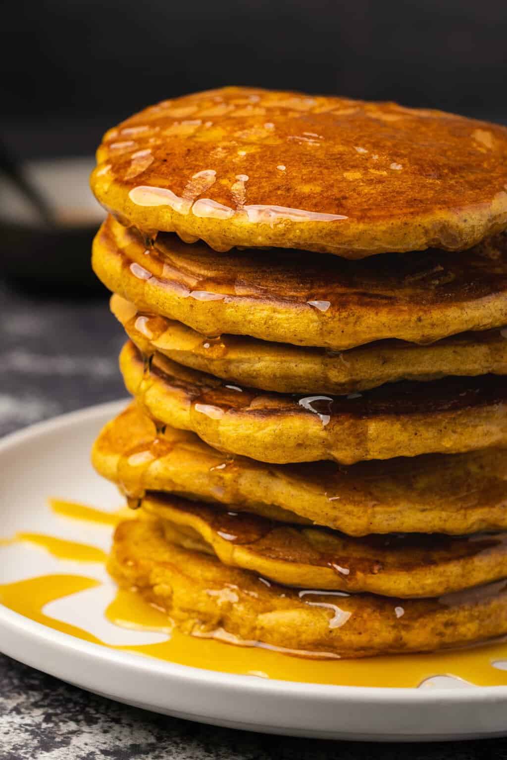 Vegan pumpkin pancakes in a stack drizzled with syrup. 