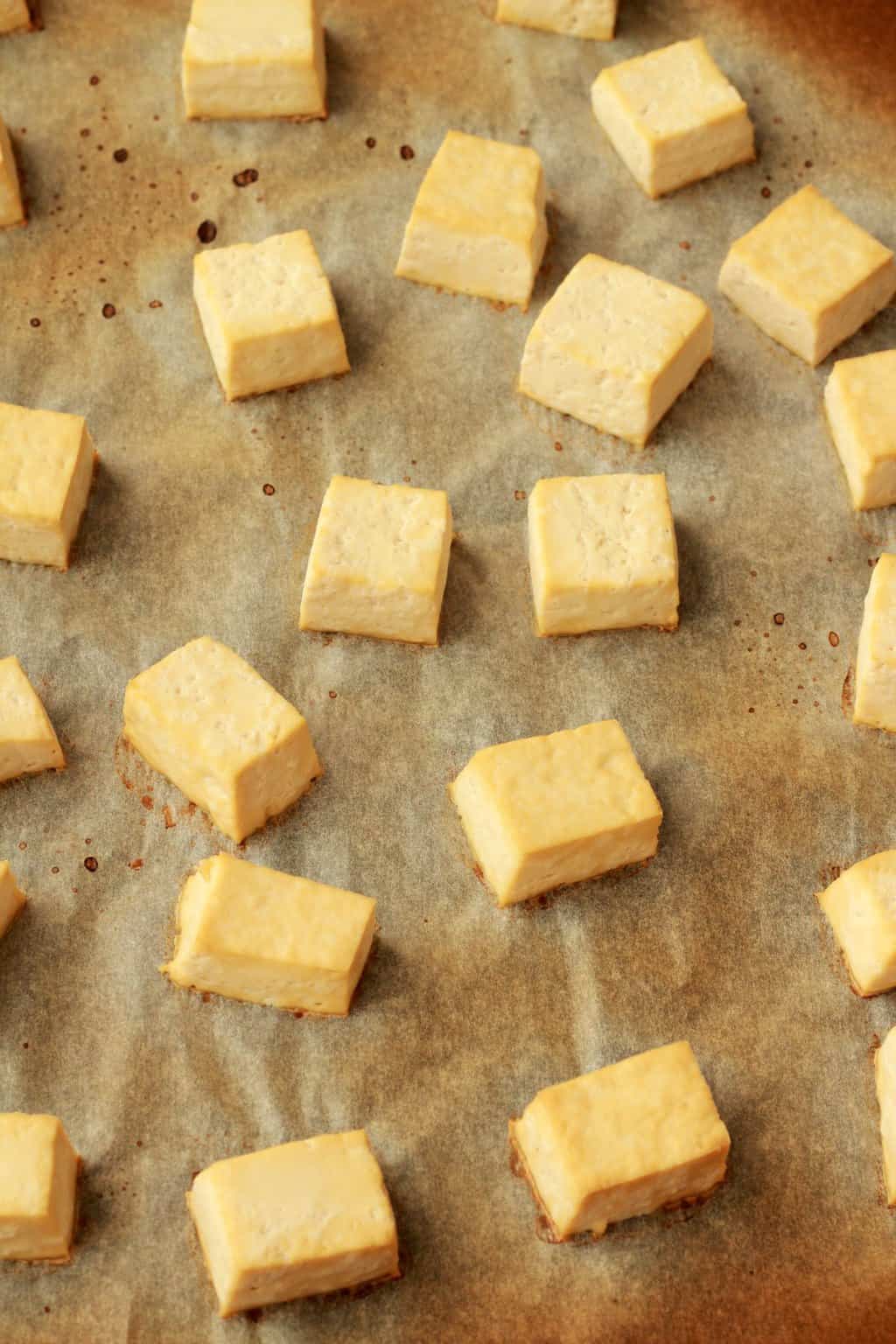 Baked tofu cubes on a parchment lined baking sheet. 