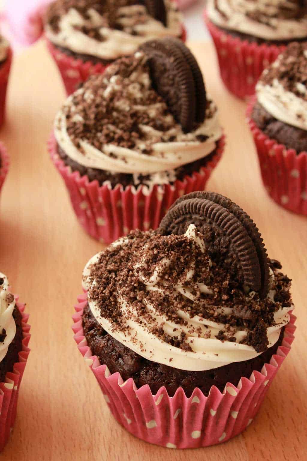 Cupcakes topped with oreo cookies and oreo sprinkles on a wooden board. 