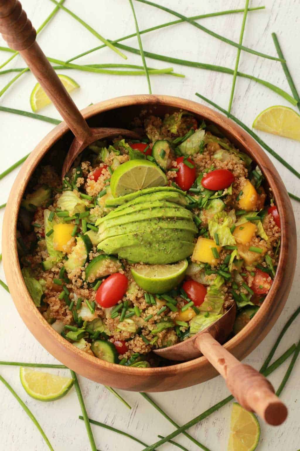 Vegan quinoa salad topped with fresh lime and avocado in a wooden salad bowl with salad spoons. 