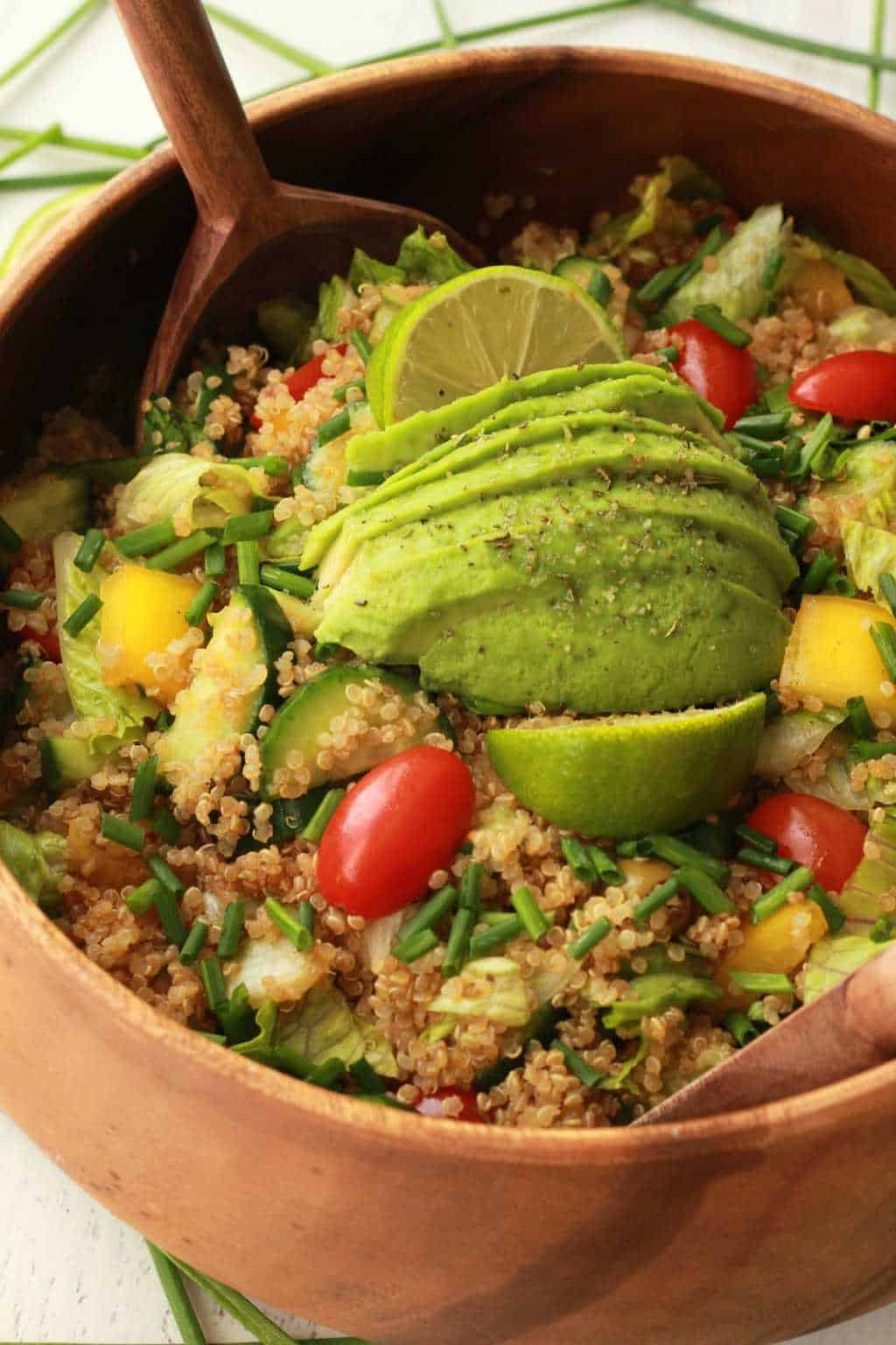 Vegan quinoa salad topped with fresh lime and sliced avocado in a wooden salad bowl with salad spoons. 