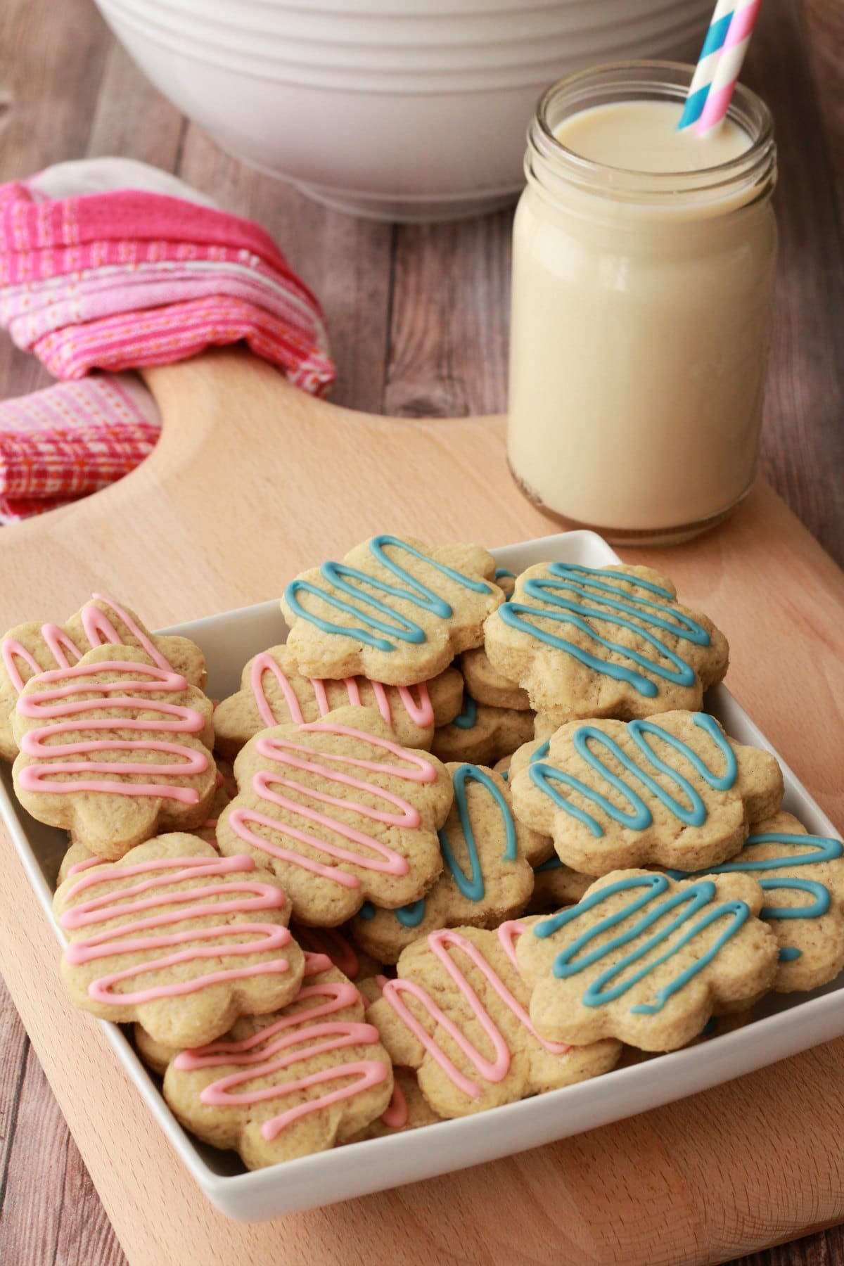Vegan sugar cookies drizzled with pink and blue frosting in a white bowl. 