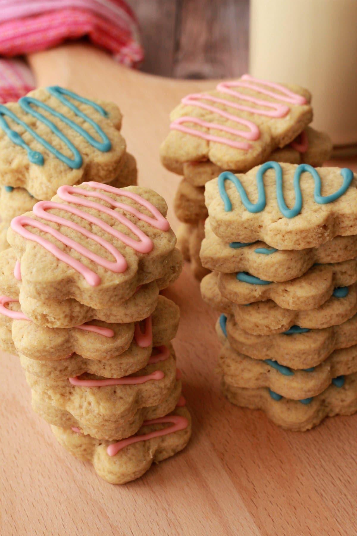 Stacks of vegan sugar cookies drizzled with pink and blue frosting. 