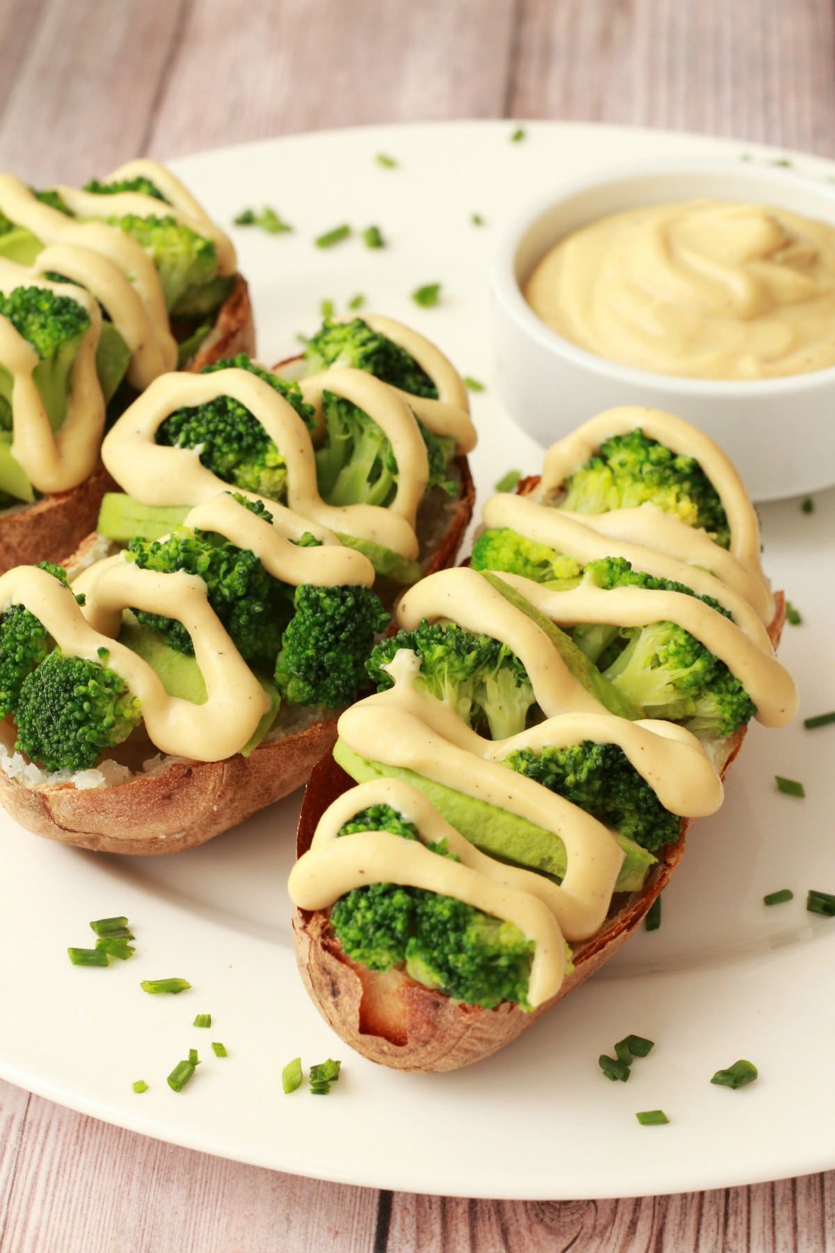 Cashew cheese sauce drizzled over baked potatoes and broccoli on a white plate. 