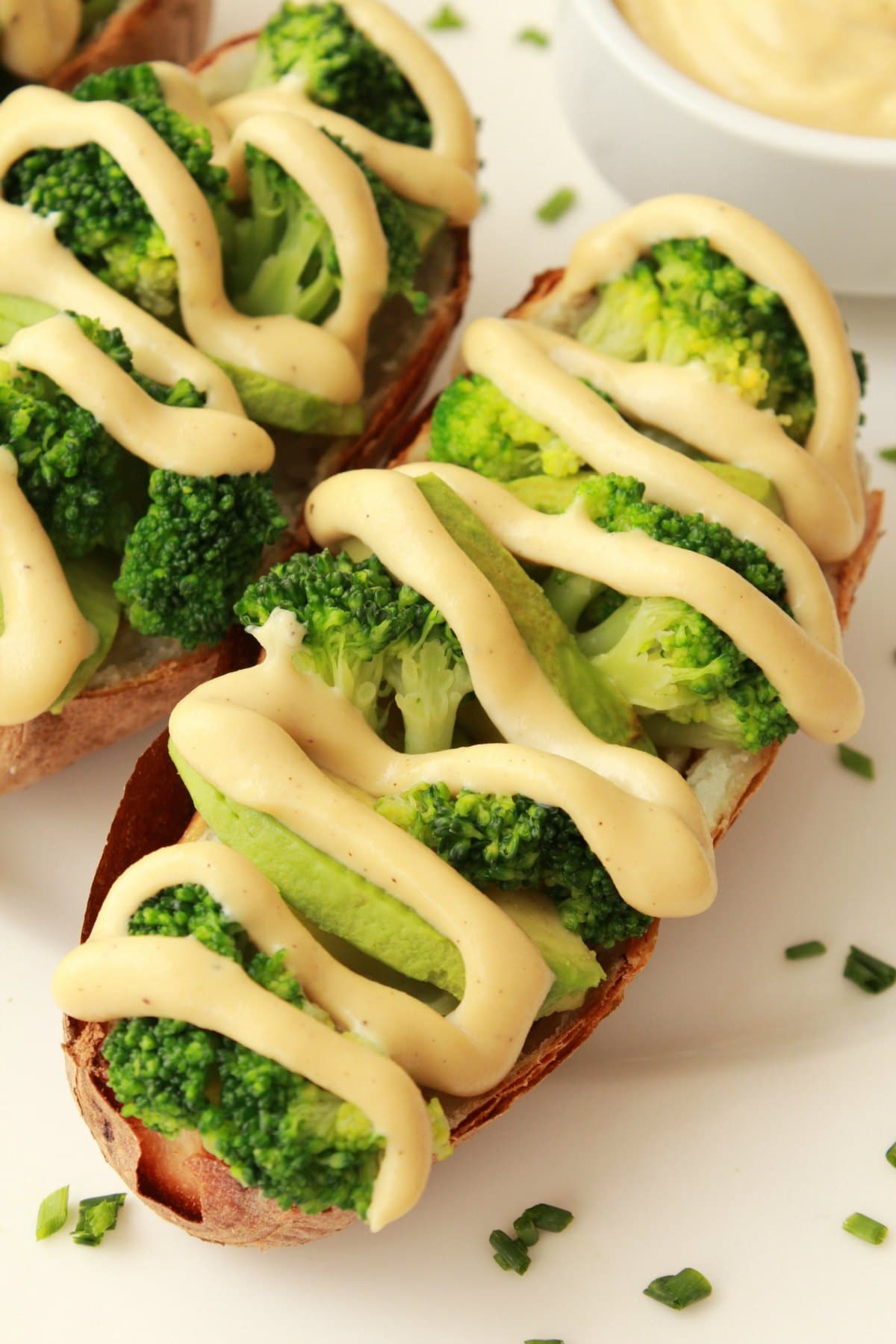 Cashew cheese sauce drizzled over baked potatoes, broccoli and avocado on a white plate. 