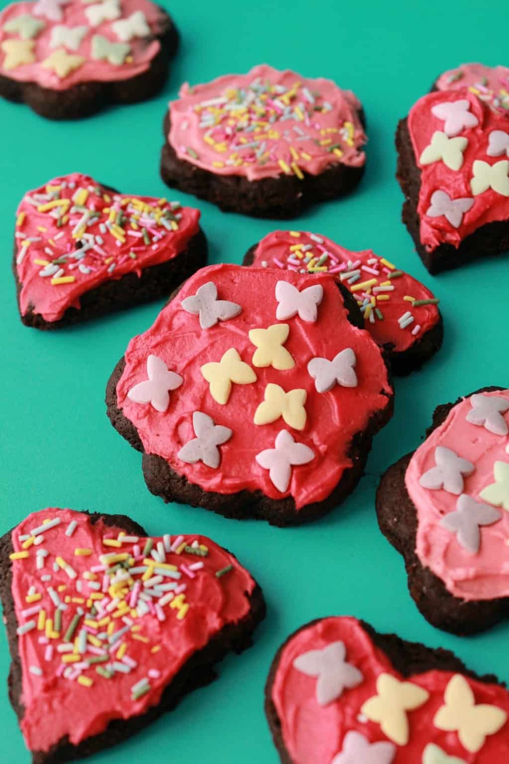 Vegan chocolate sugar cookies topped with pink frosting and sprinkles. 