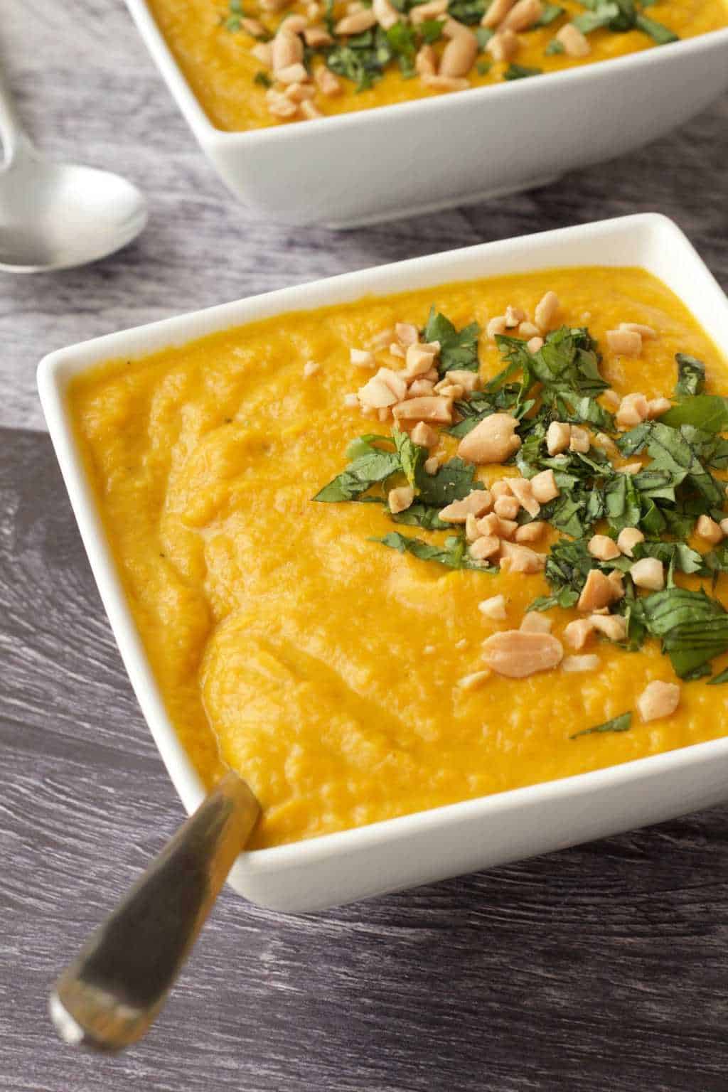 Vegan carrot soup topped with chopped cilantro and peanuts in white bowls. 
