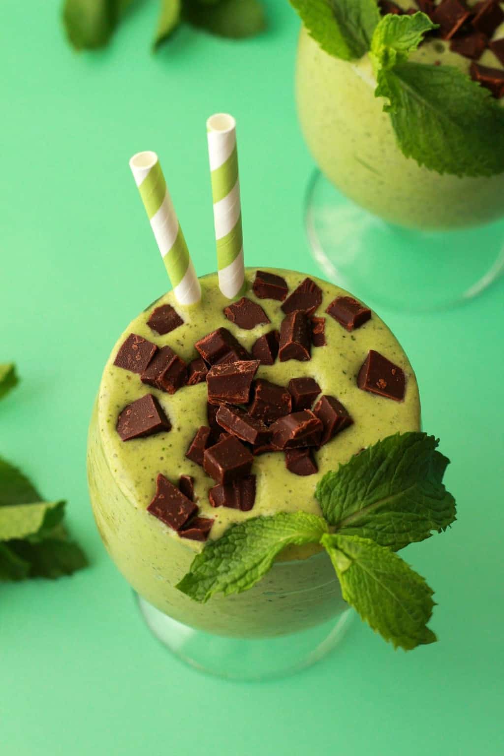 Mint smoothie with fresh mint in a glass with a green and white striped straw. 
