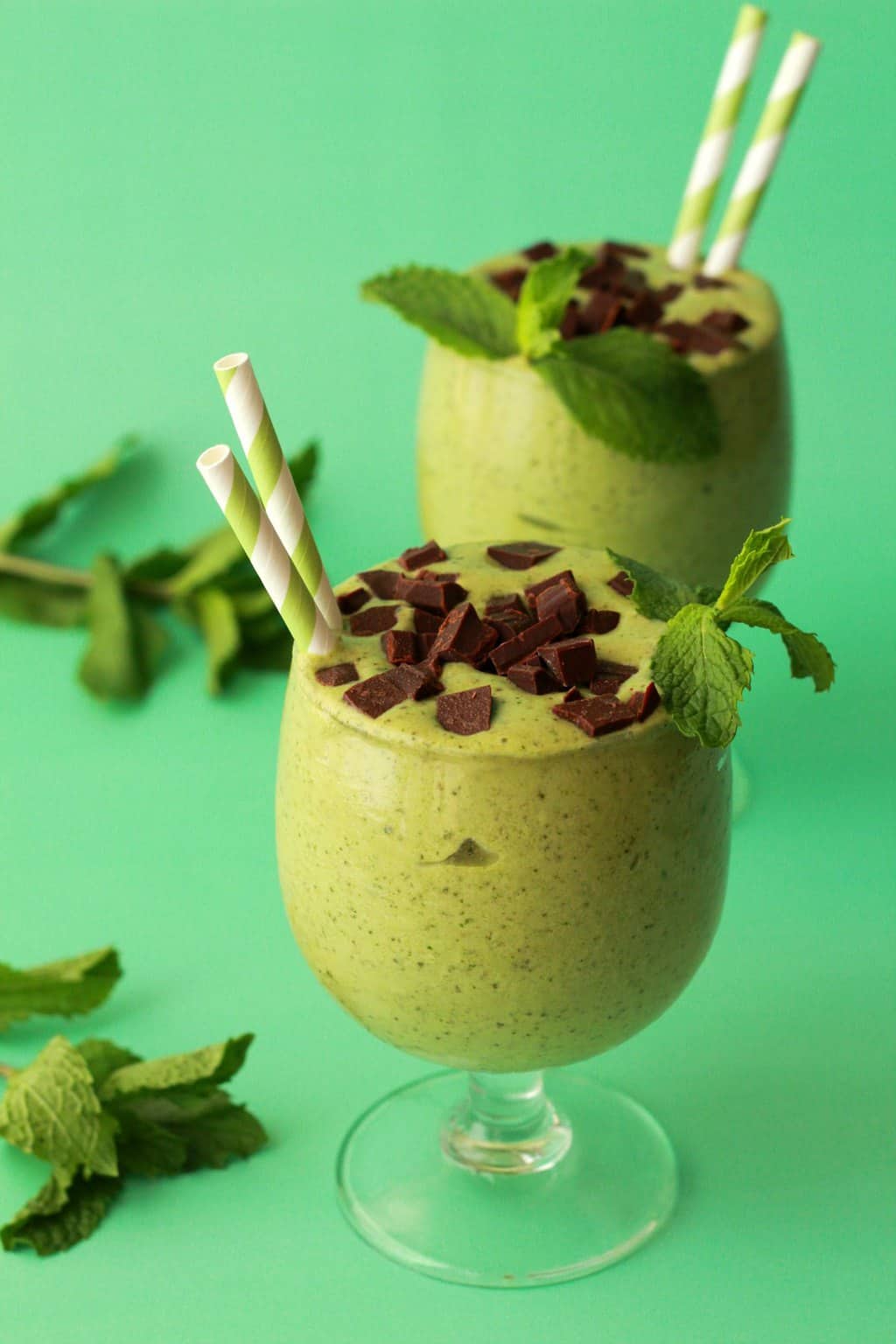 Mint smoothie in glasses with green and white striped straws. 