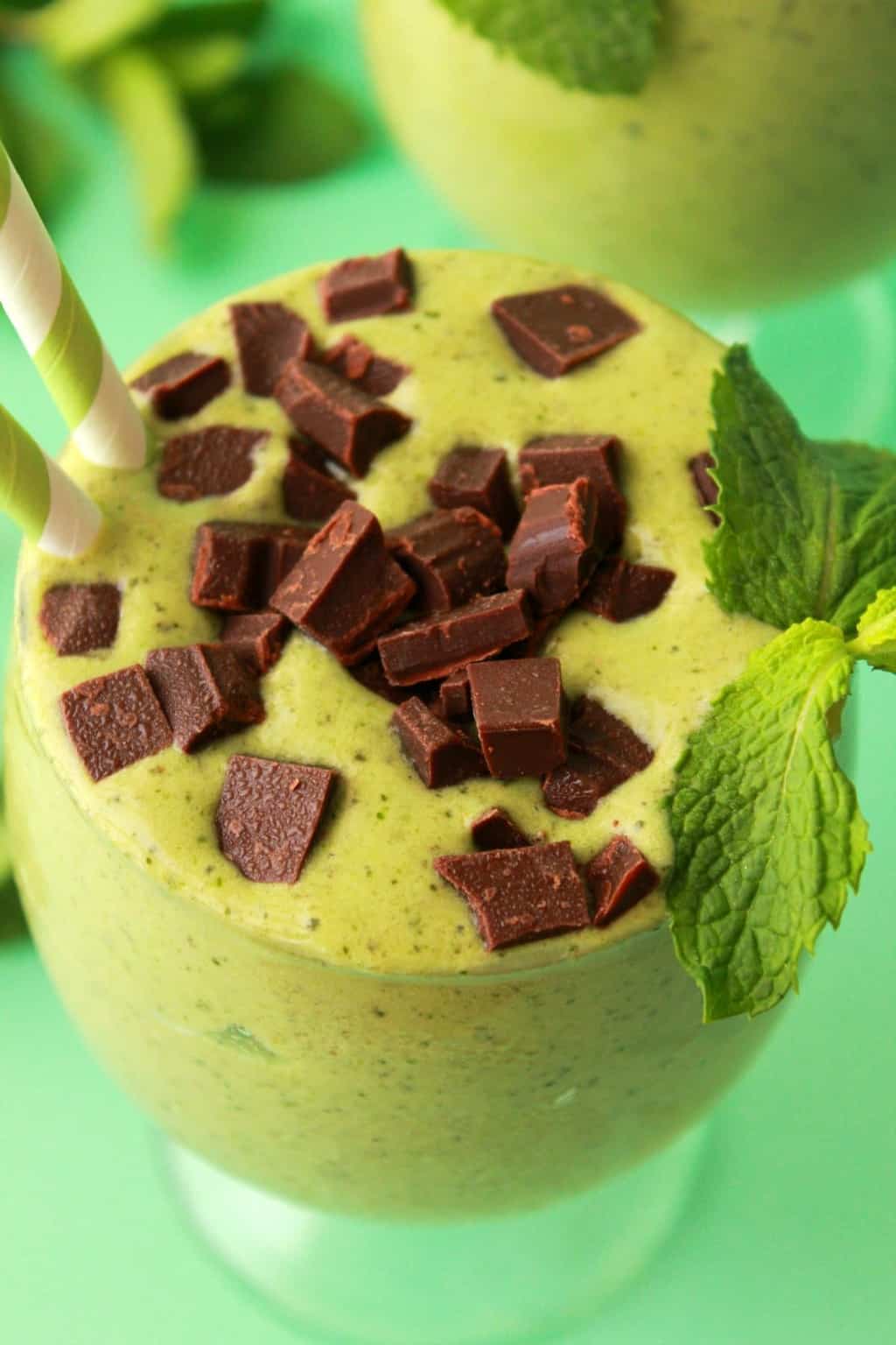 Mint chocolate chip smoothie in a glass with a green and white striped straw. 
