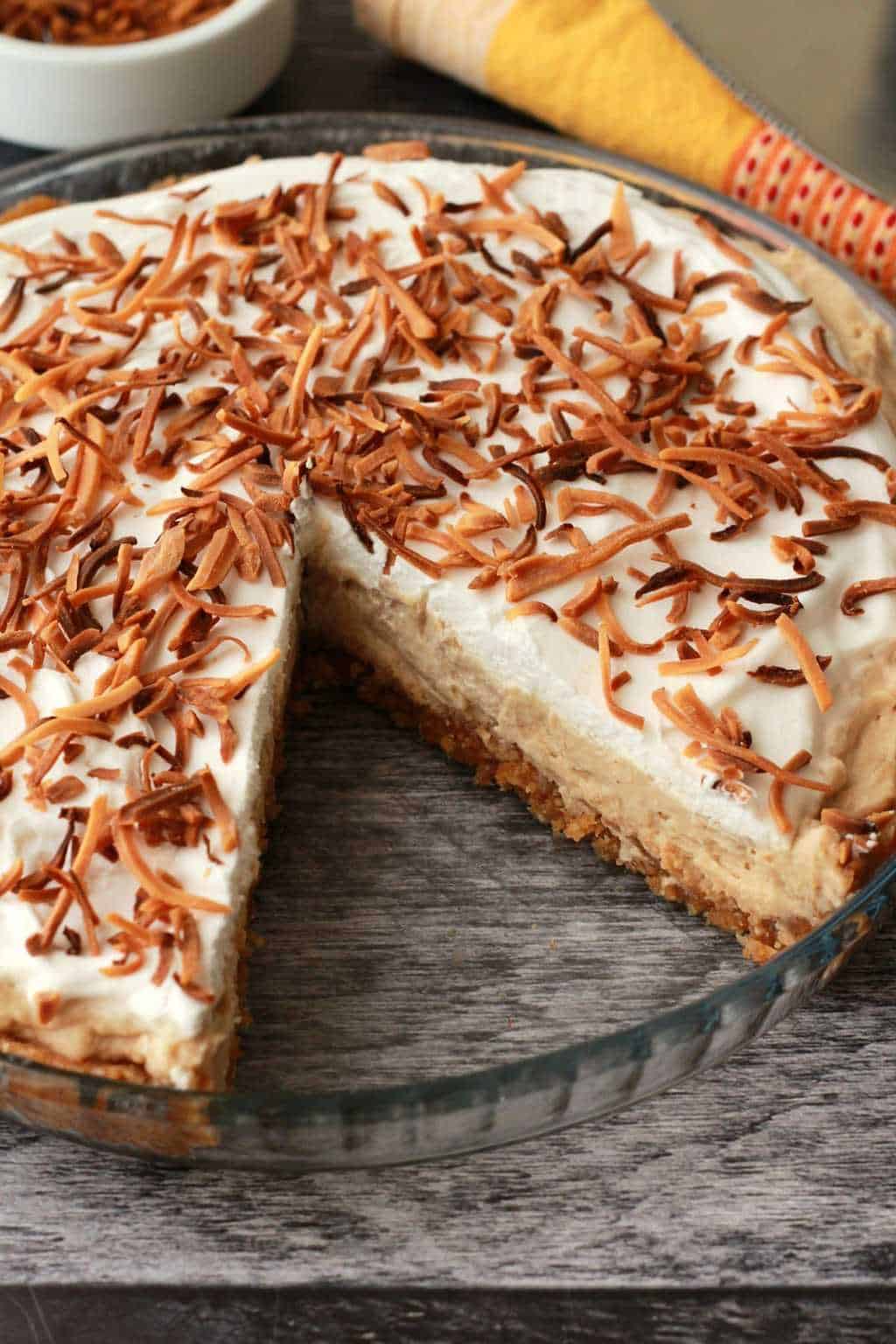 Vegan coconut cream pie in a glass pie dish with a slice cut out. 