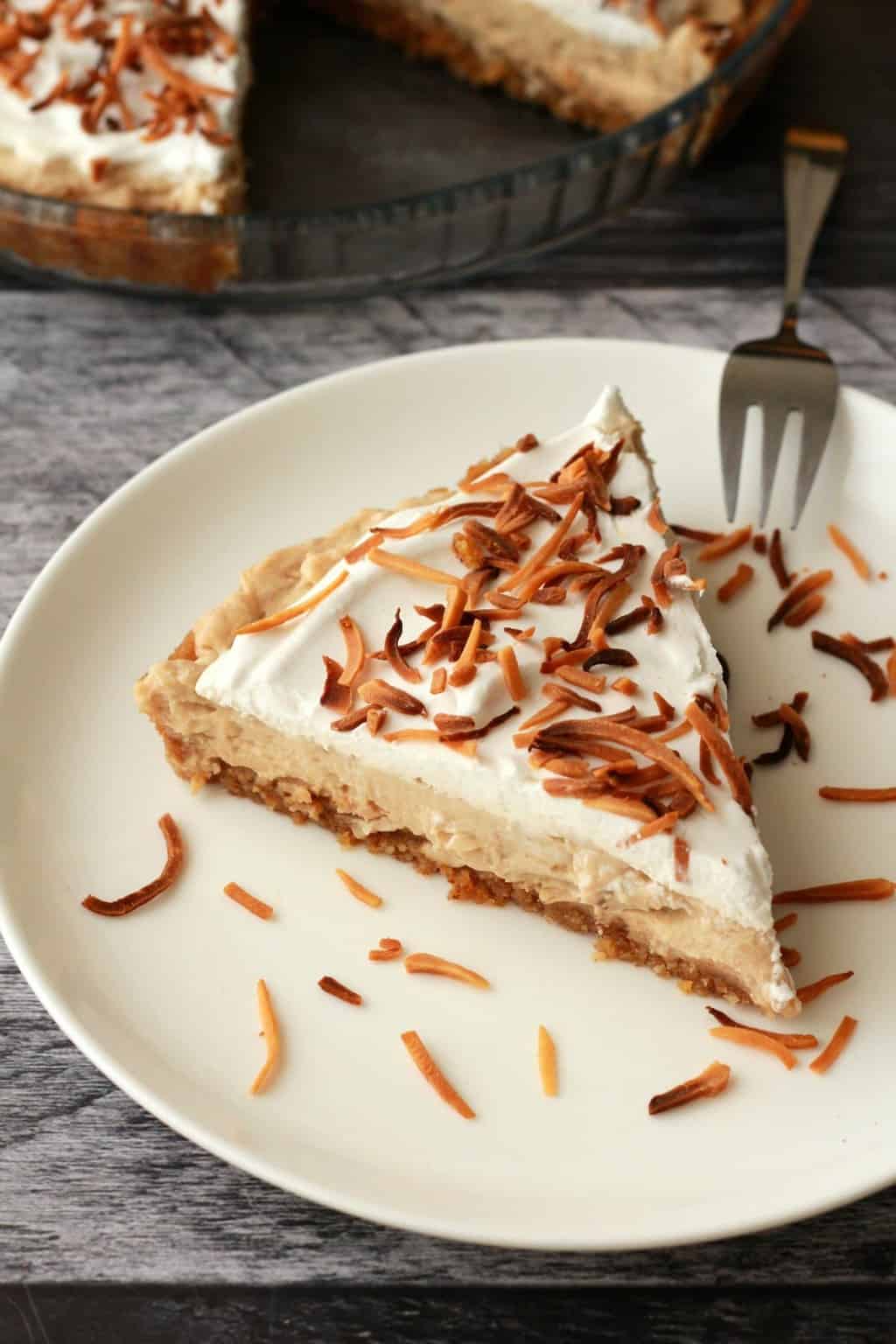 Slice of coconut cream pie on a white plate. 