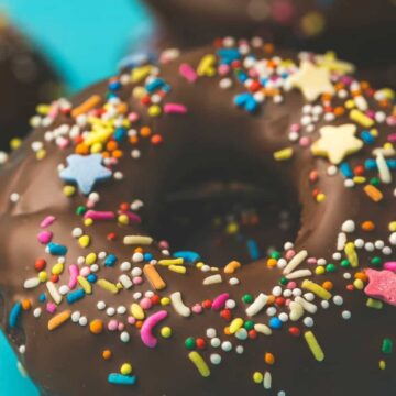 Vegan chocolate donuts topped with melted chocolate and sprinkles.
