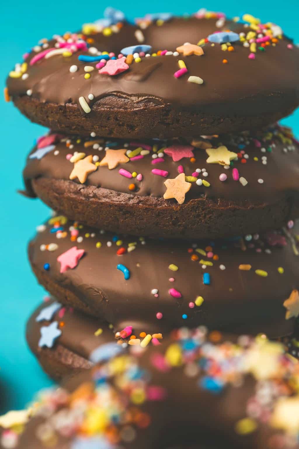 Vegan chocolate donuts topped with chocolate and sprinkles in a stack. 
