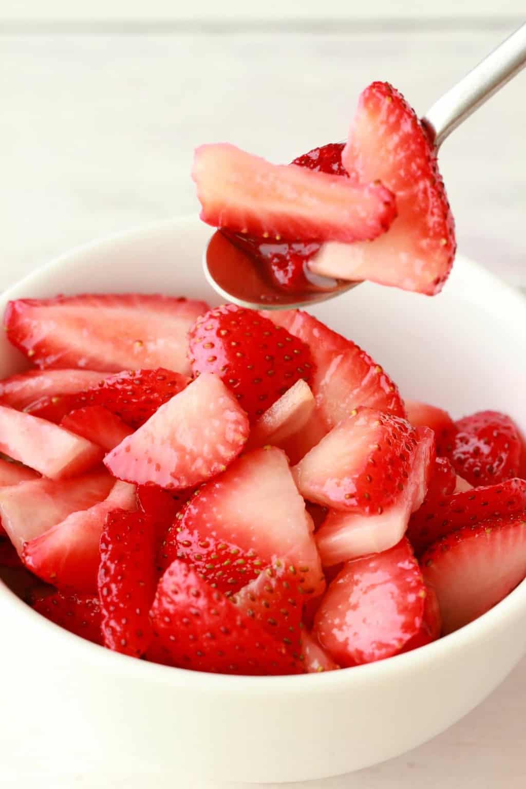 Sliced Strawberries in a white bowl with a spoon. 