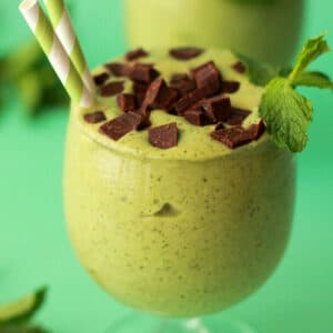 Mint chocolate chip smoothie in a glass with a green and white striped straw.