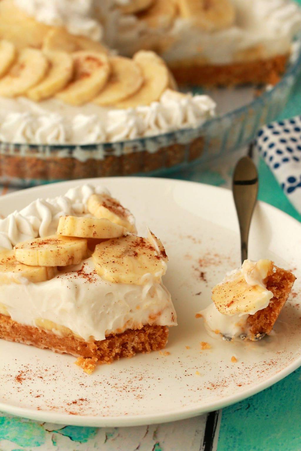 A slice of vegan banana cream pie on a white plate with a cake fork. 