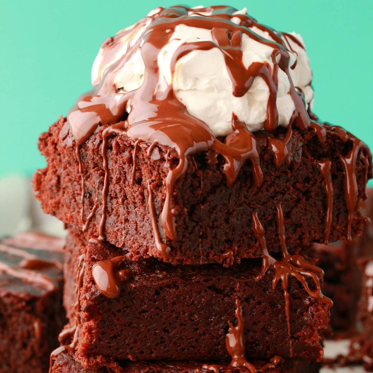 Stack of vegan brownies topped with vegan whipped cream and melted chocolate.