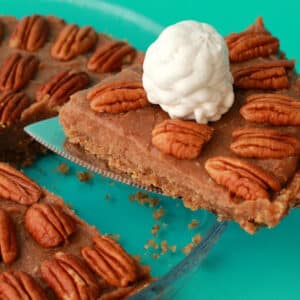 Raw vegan pecan pie in a glass pie dish with one slice cut and ready to serve.