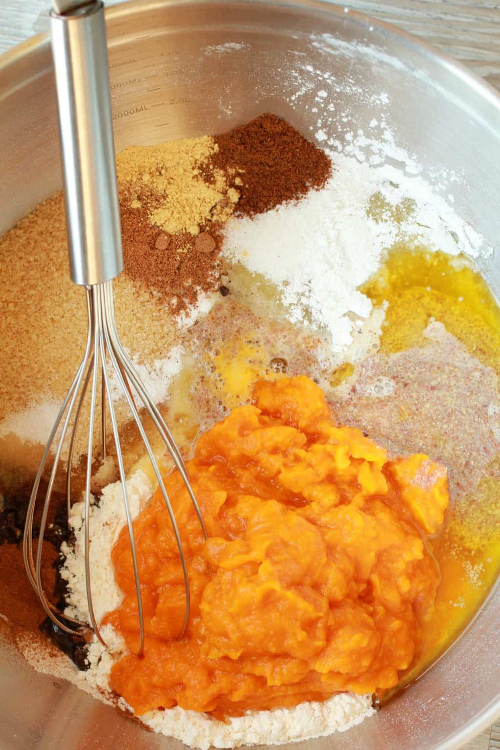 Ingredients for a vegan pumpkin cake in a silver mixing bowl with a whisk. 
