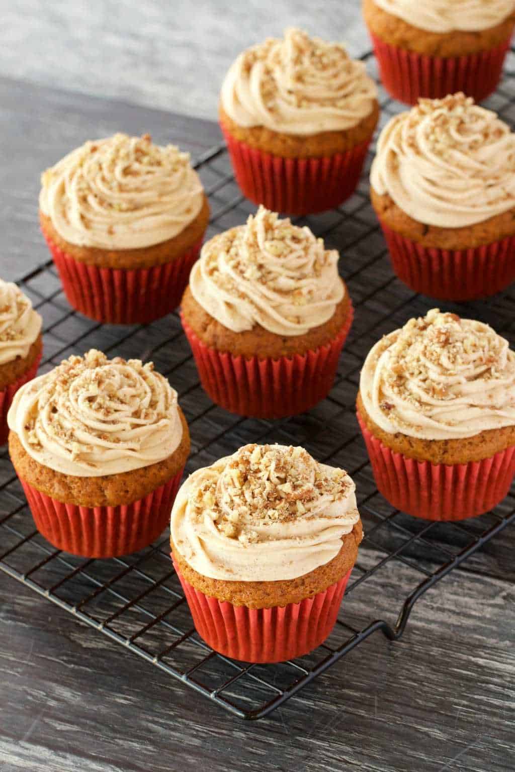 Vegan pumpkin cupcakes topped with a pumpkin spice frosting on a wire cooling rack. 