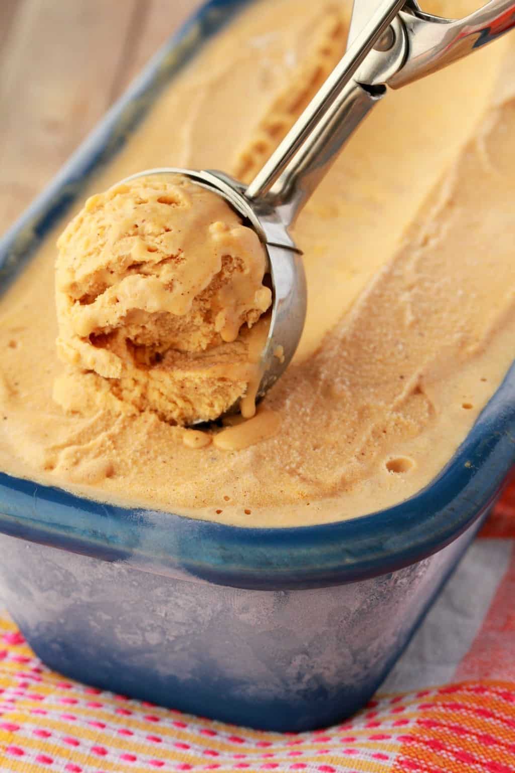 Vegan pumpkin ice cream in a blue ceramic loaf pan with an ice cream scoop. 