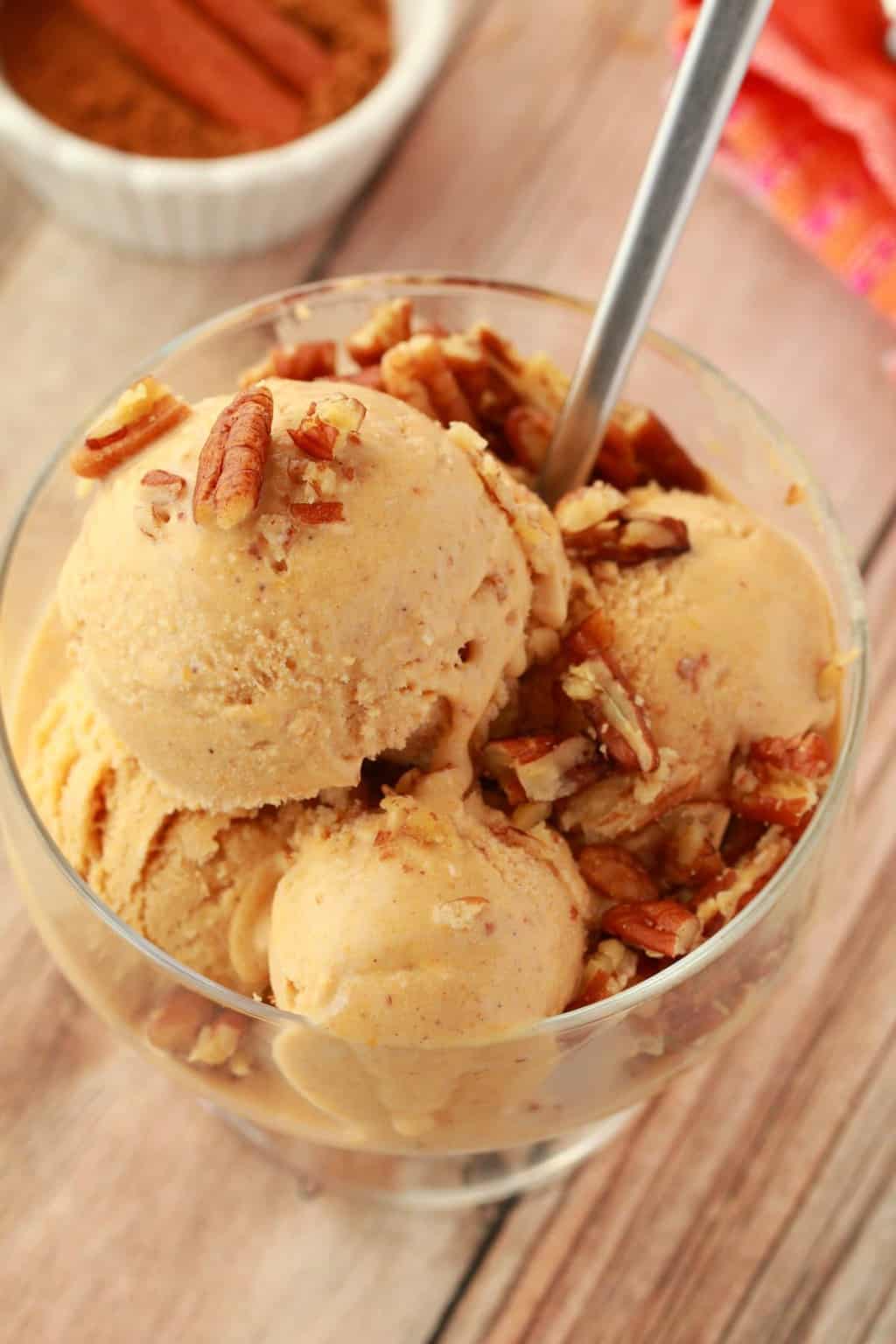 Vegan pumpkin ice cream topped with pecan nuts in a glass bowl with a spoon. 