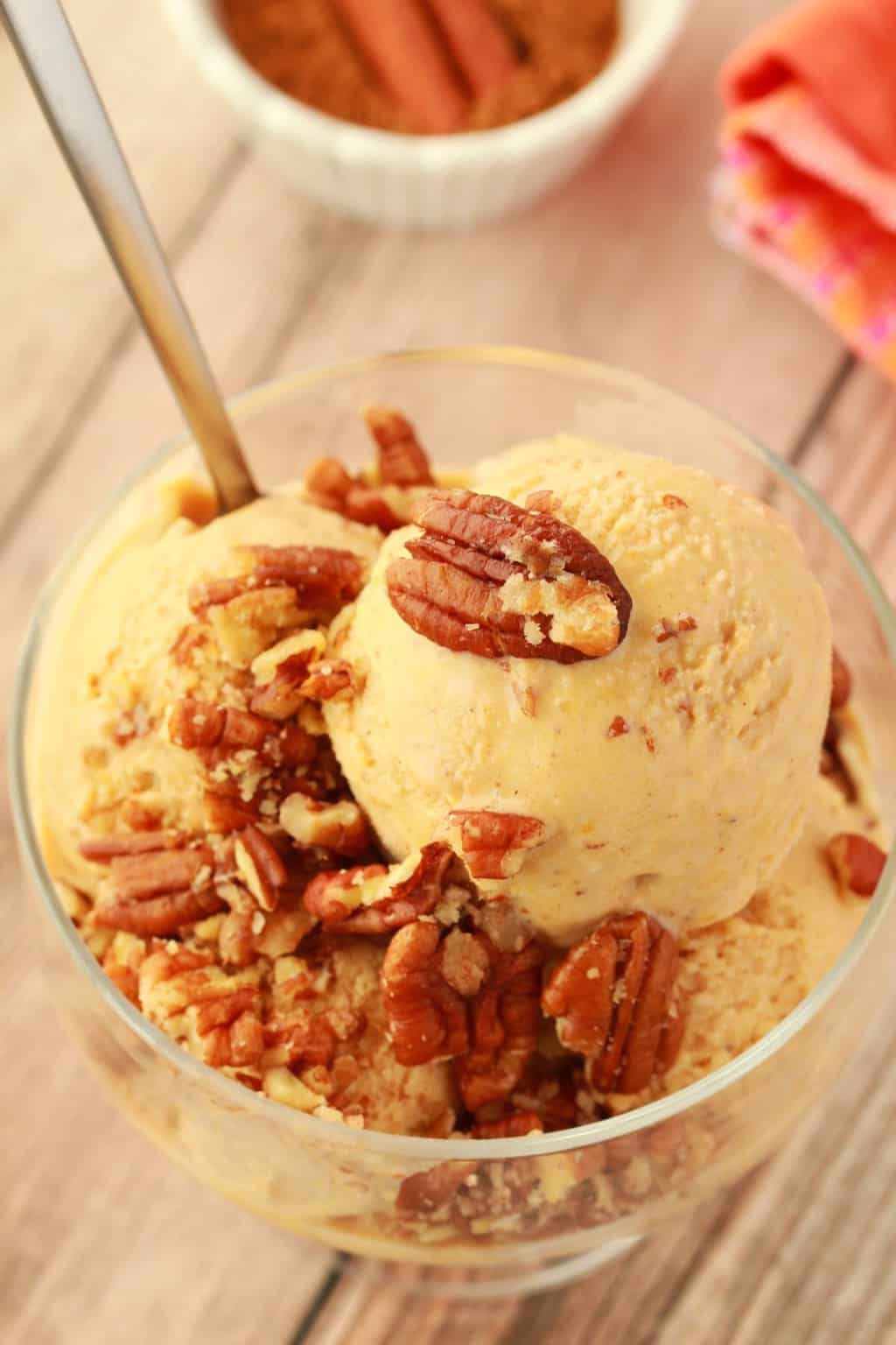 Vegan pumpkin ice cream topped with pecans in a glass bowl with a spoon. 