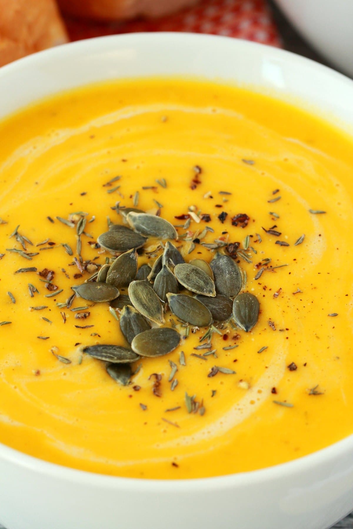 Vegan pumpkin soup topped with pumpkin seeds in a white bowl. 