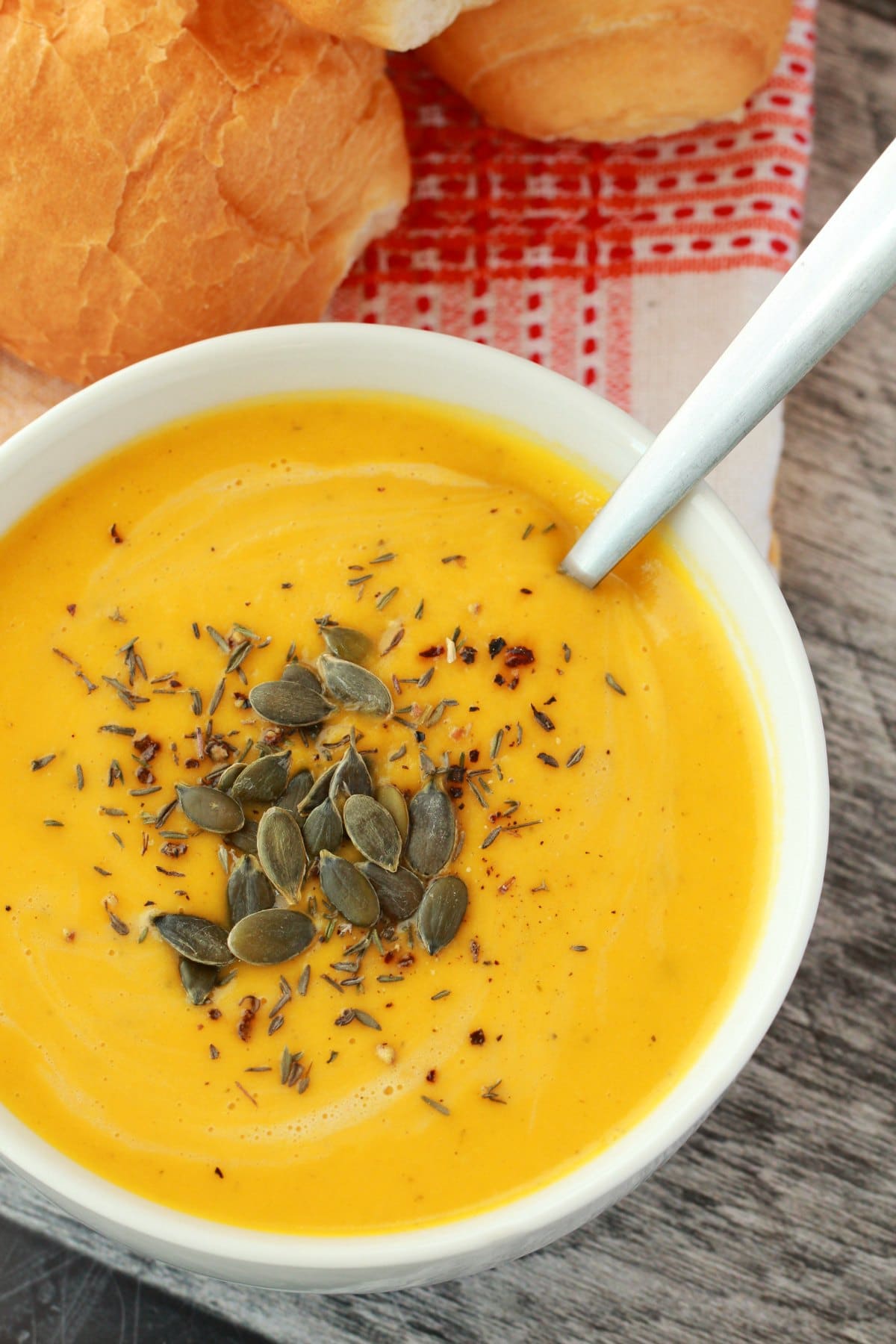 Vegan pumpkin soup topped with dried thyme and pumpkin seeds in a white bowl. 