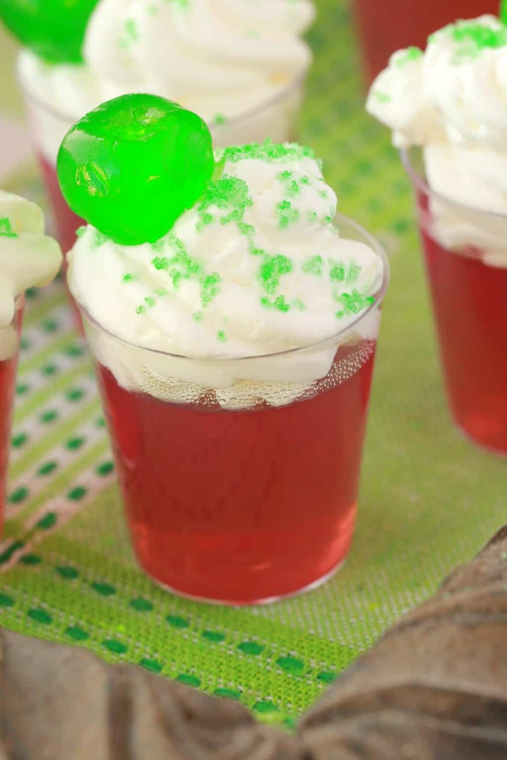 Vegan jello shots topped with vegan whipped cream, green sanding sugar and a green cherry. 