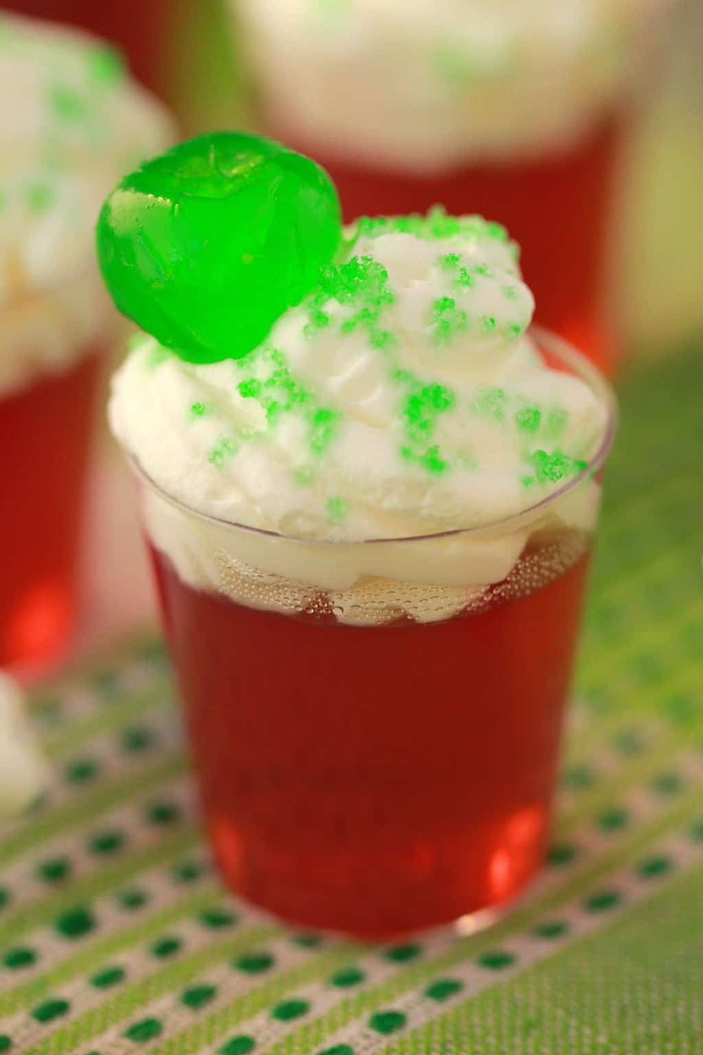 Vegan jello shots topped with vegan whipped cream, green sanding sugar and a green cherry. 