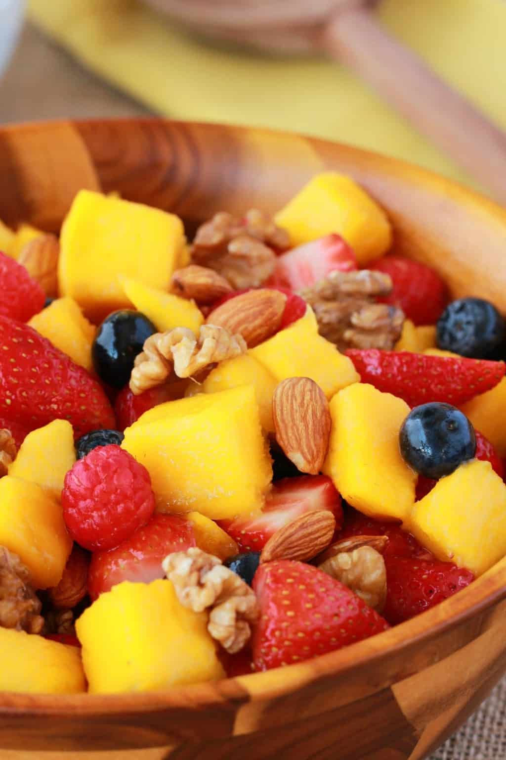 Chopped mango with other fruits and nuts in a wooden bowl. 