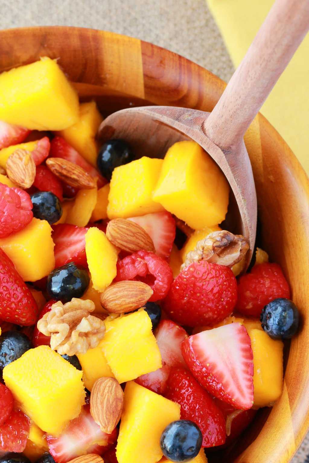 Mango, strawberries, raspberries and blueberries with nuts in a wooden bowl. 
