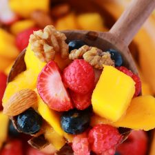 Mango berry fruit salad in a wooden bowl with a spoon.