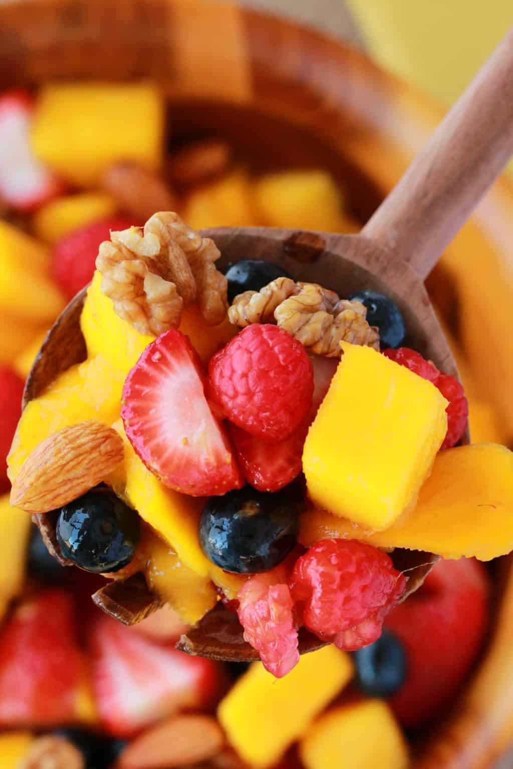 Chopped fruits with nuts in a wooden bowl with a wooden serving spoon. 