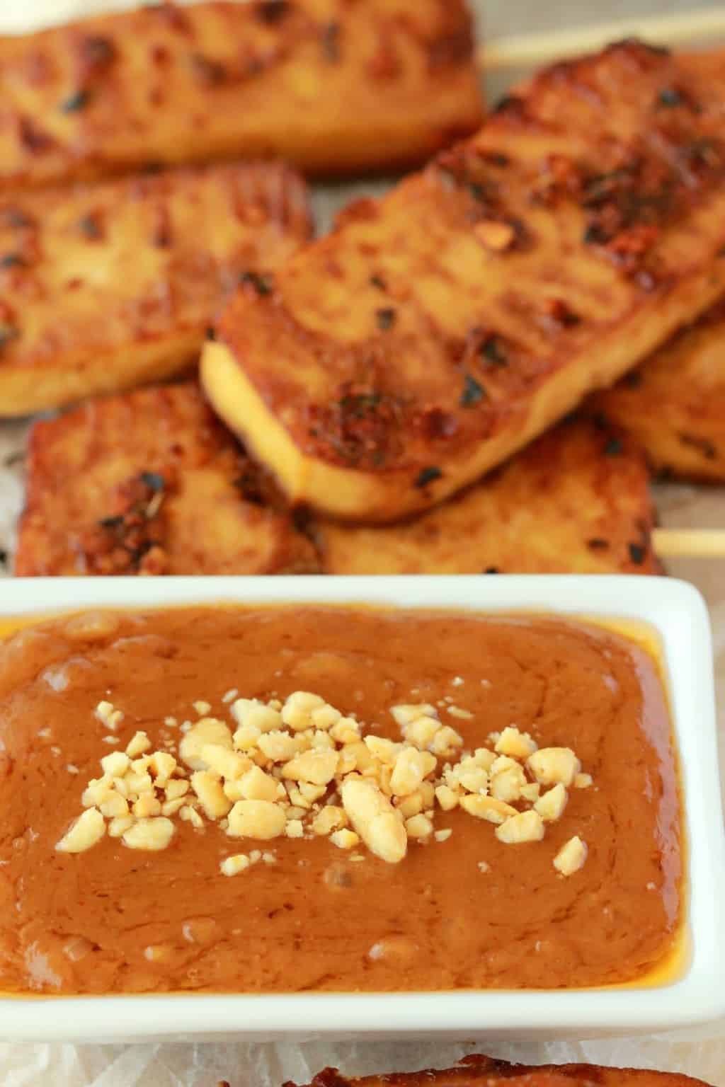 Baked tofu satay with peanut sauce in a white dish. 