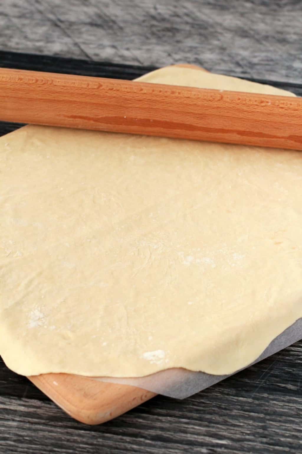 Rolled out pizza dough on a wooden board with a rolling pin on top