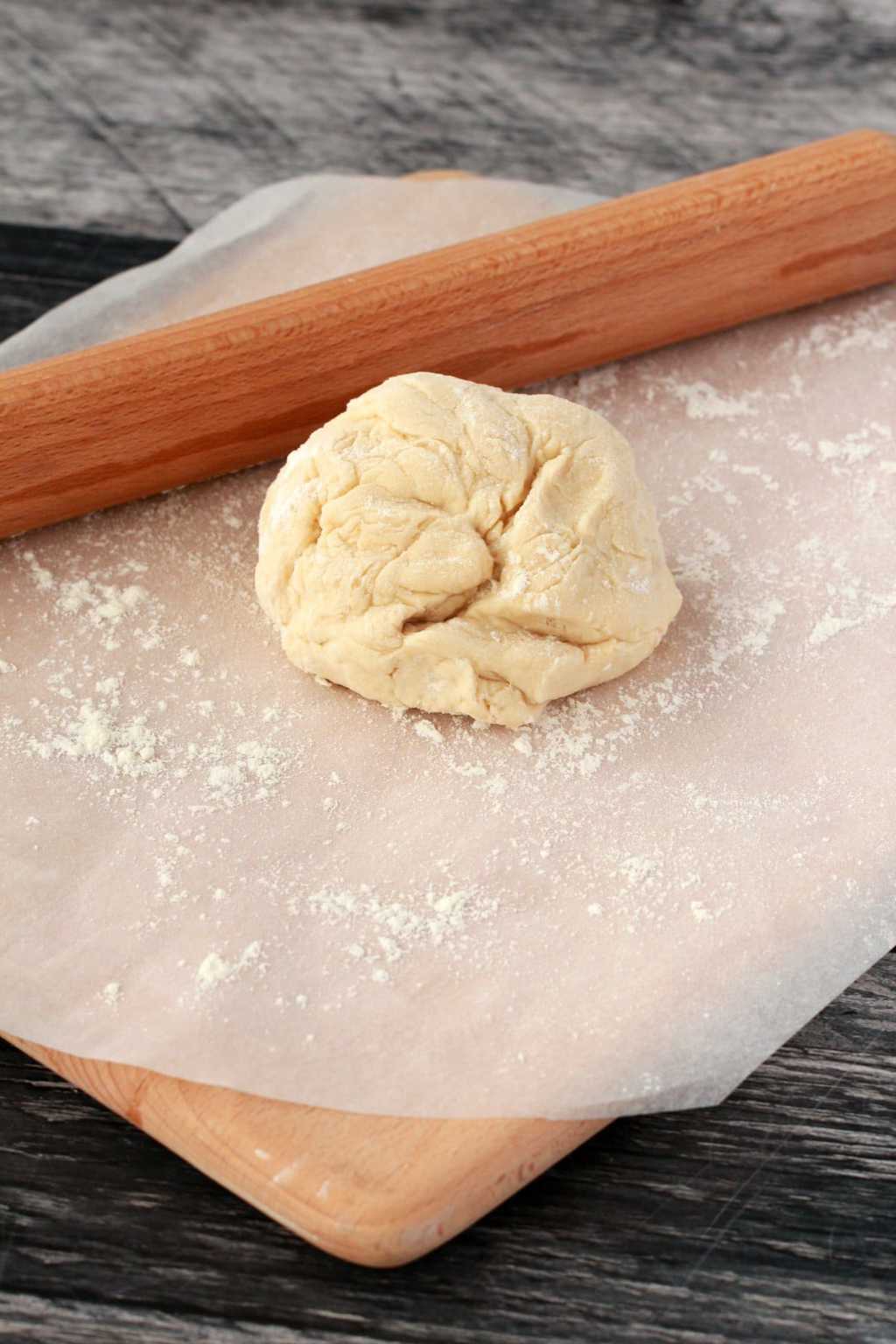 A ball of pizza dough on a piece of parchment paper with a rolling pin nearby