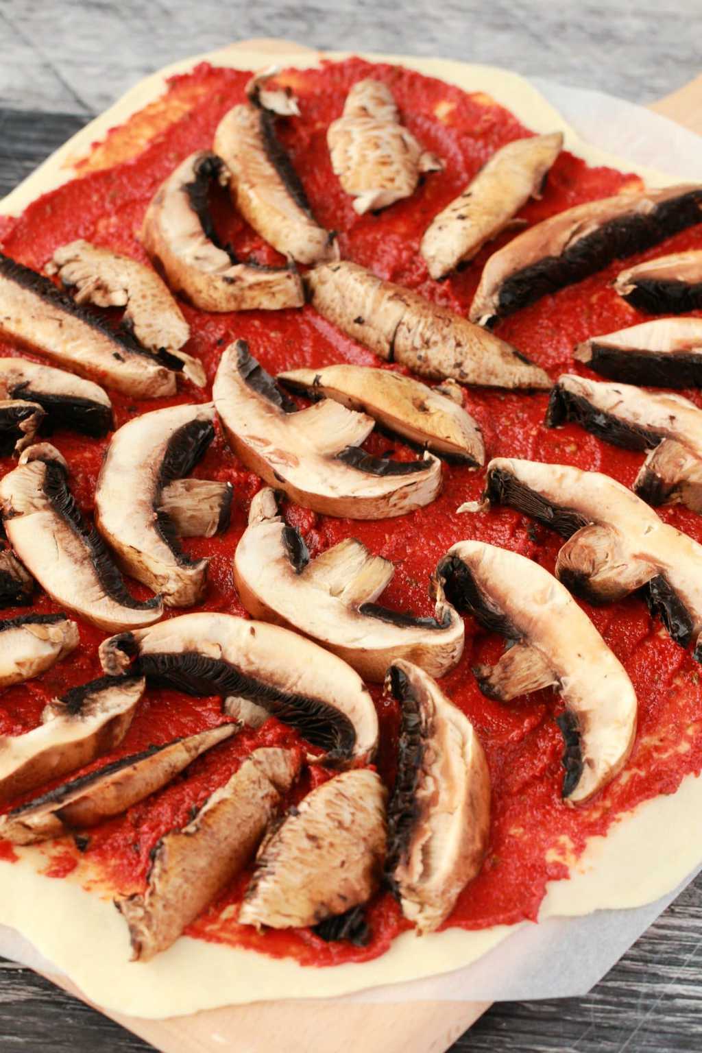 A pizza base with tomato sauce and mushrooms ready to go into the oven