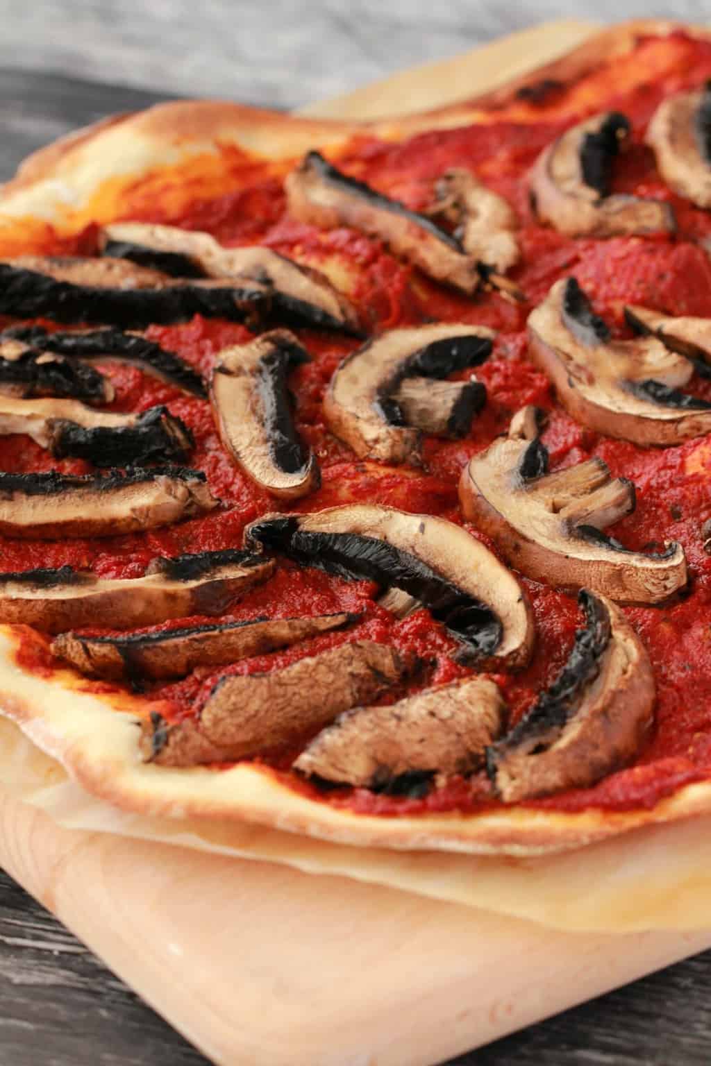 Just cooked pizza base with tomato sauce and black mushrooms on a wooden board