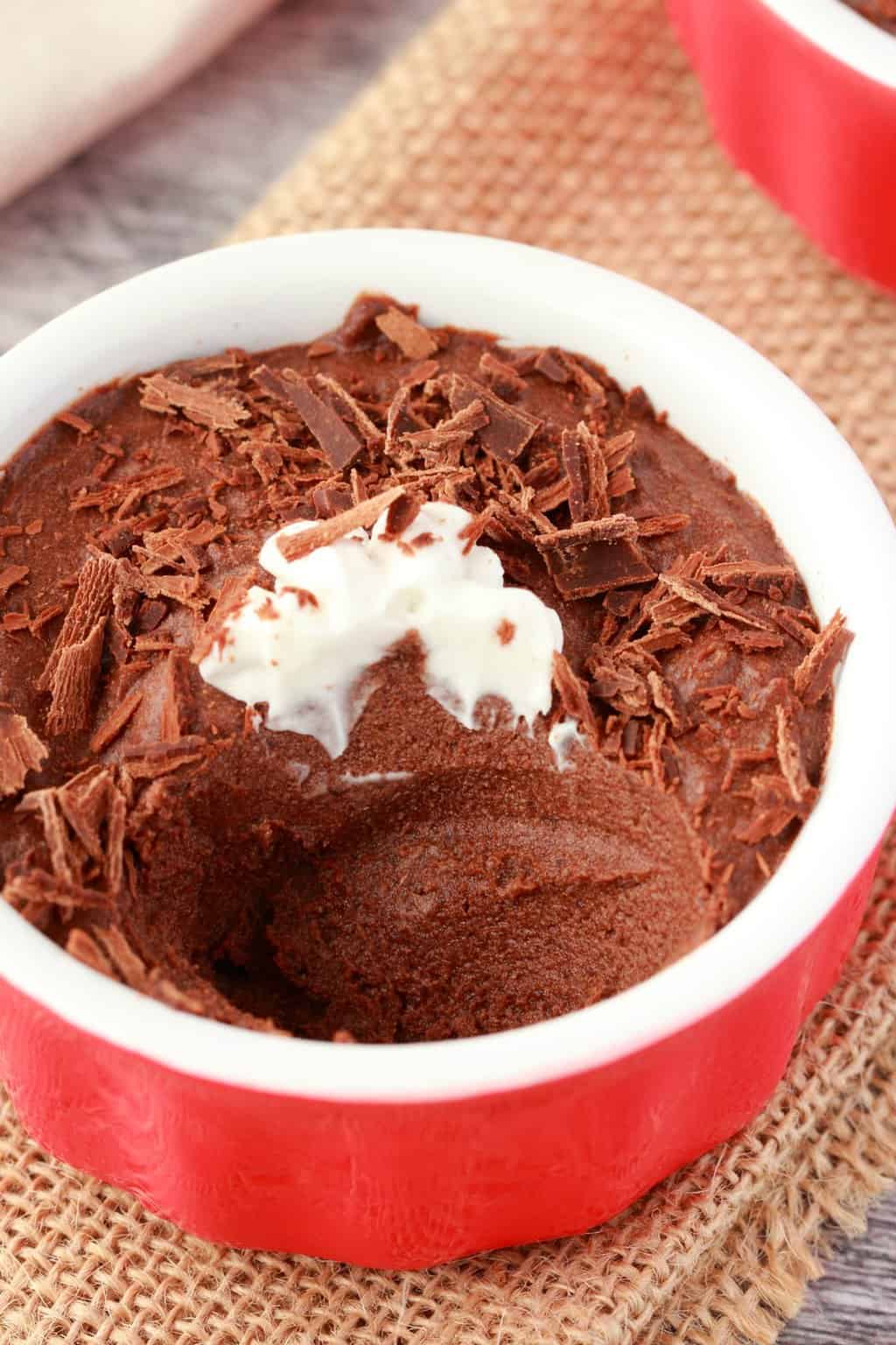Vegan mousse topped with cream and chocolate shavings in a red and white ramekin.