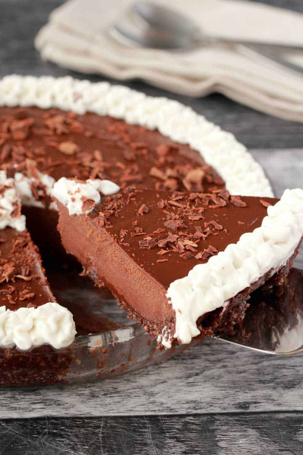 Vegan chocolate pie decorated with whipped coconut cream and chocolate flakes in a glass pie dish. 