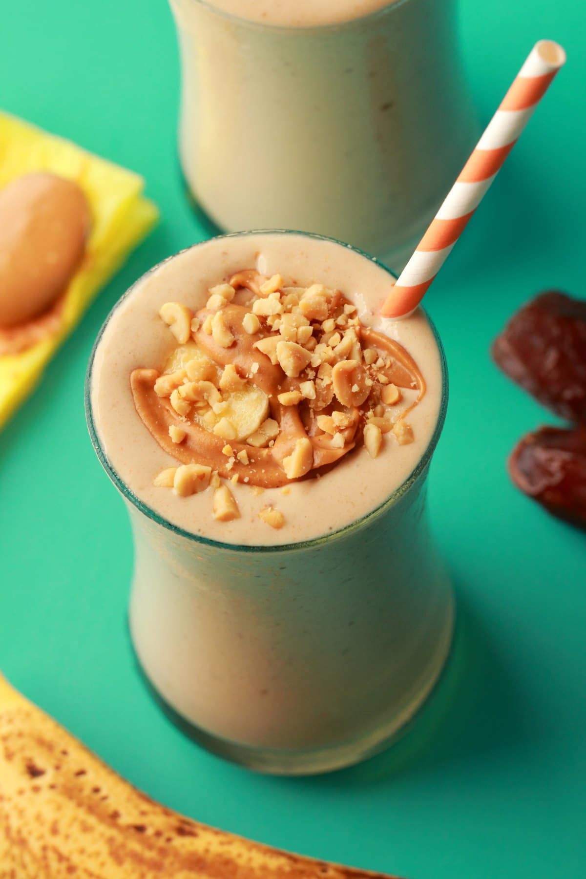 Peanut Butter Banana Smoothie on a green background with medjool dates, a banana and a spoonful of peanut butter.