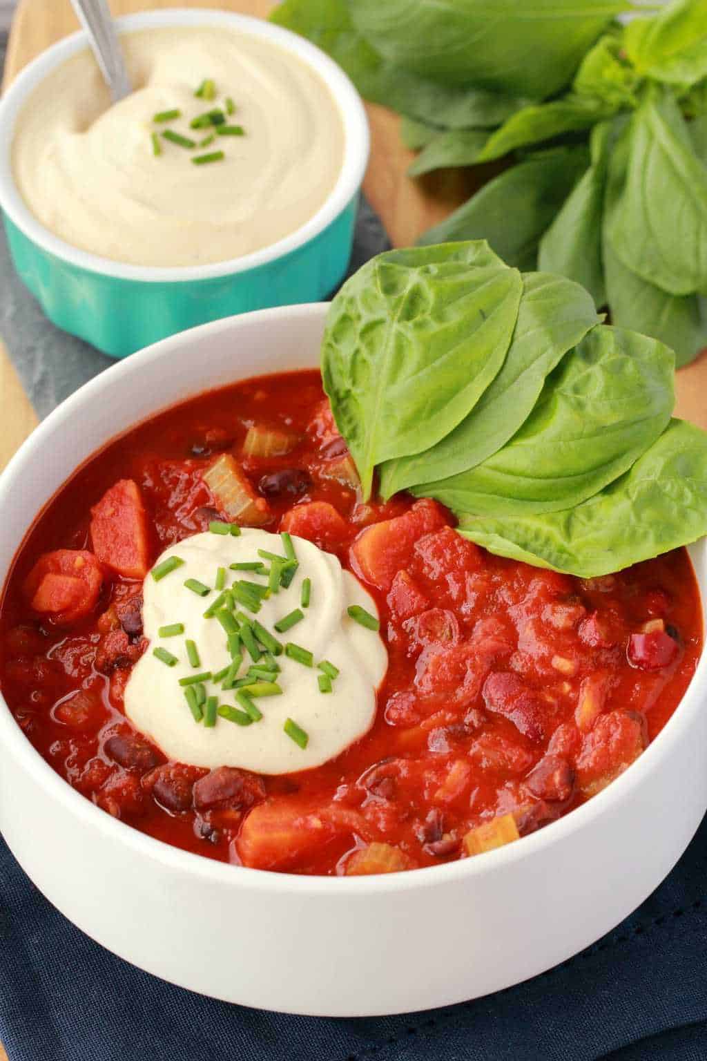 Vegan chili topped with cashew cream, fresh chives and fresh basil in a white bowl. 