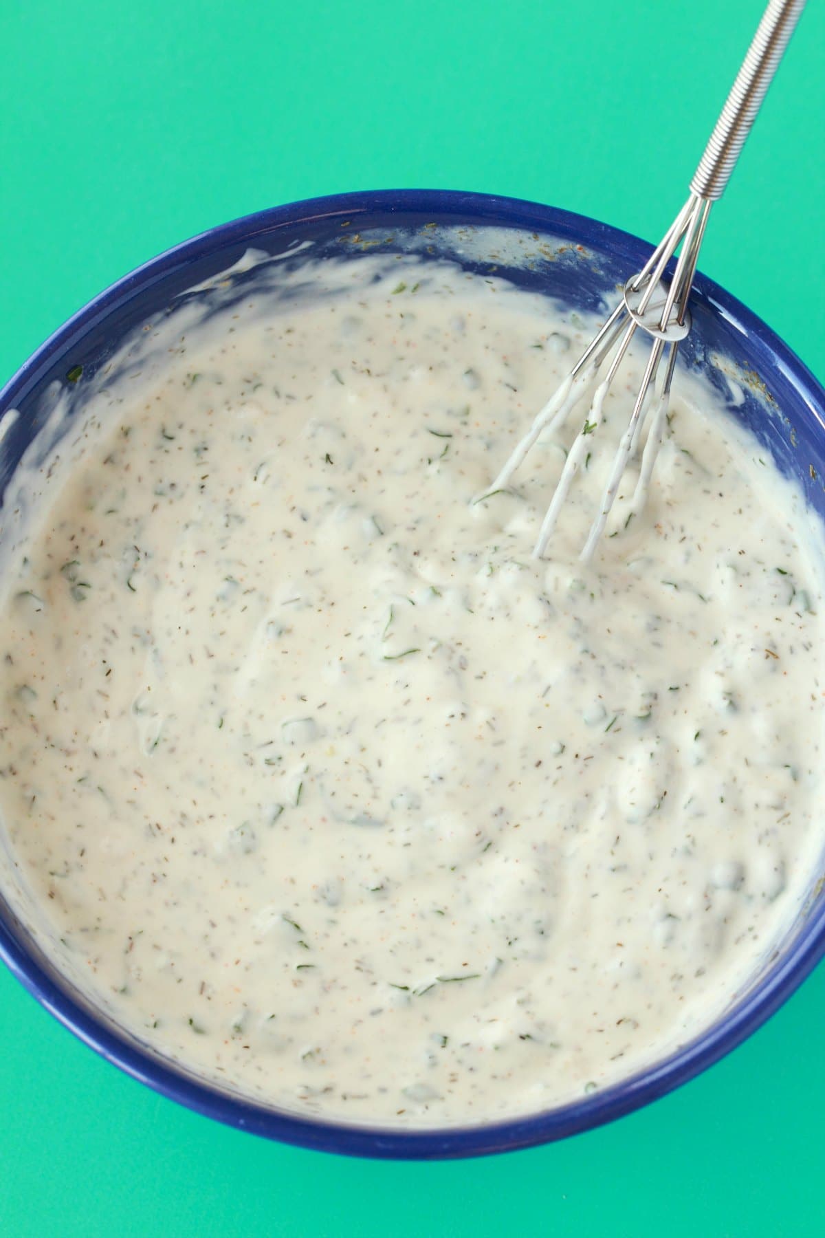 Freshly mixed vegan ranch dressing in a blue bowl with a whisk. 