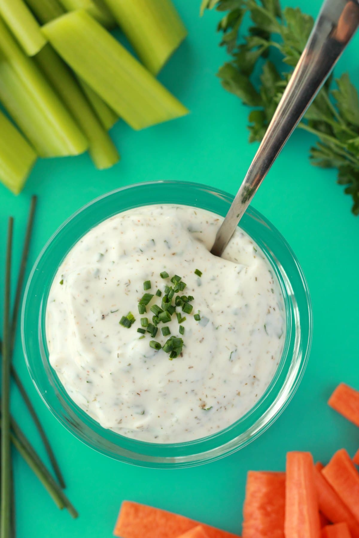 Vegan ranch dressing topped with chopped chives in a glass jar with a spoon.