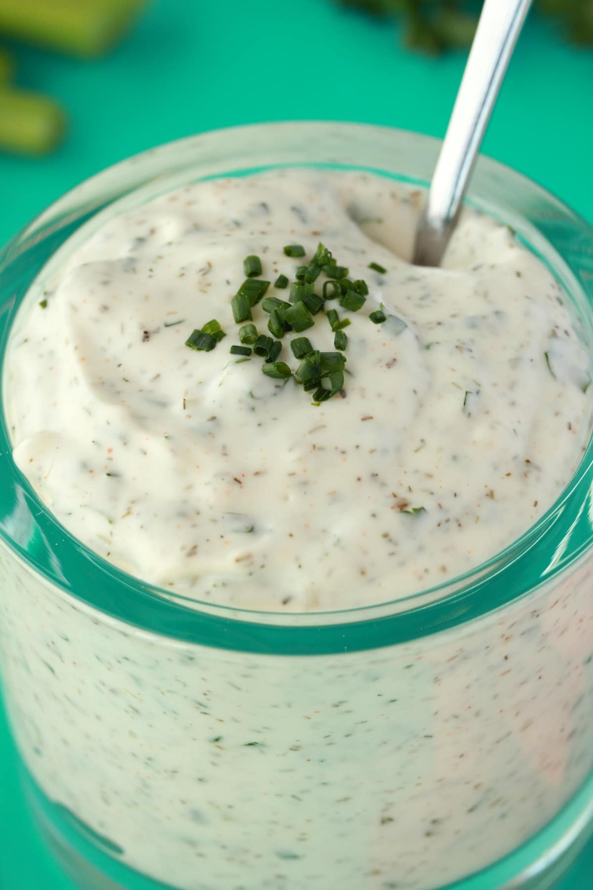 Vegan ranch dressing topped with chopped chives in a glass bowl with a spoon. 