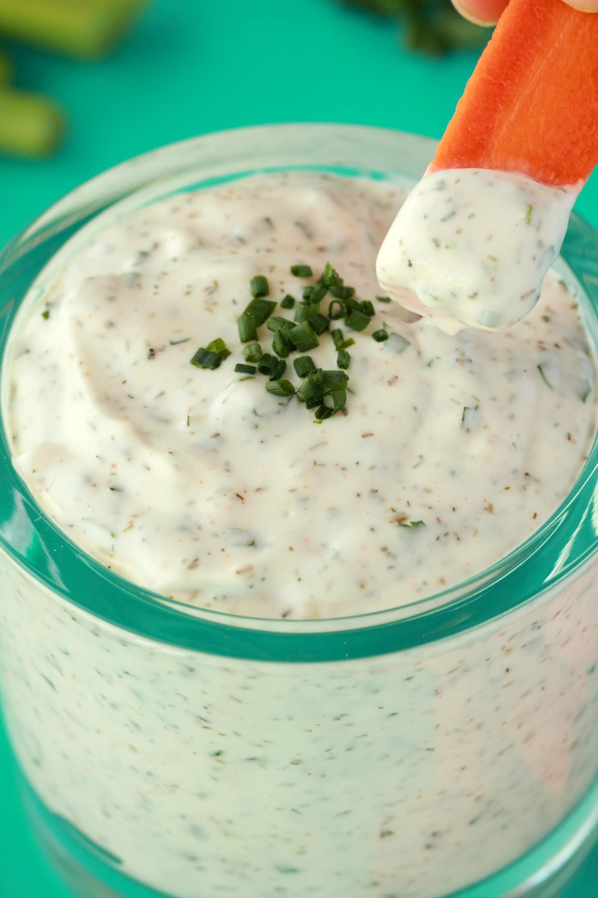 A carrot dipping into vegan ranch dressing in a glass jar. 